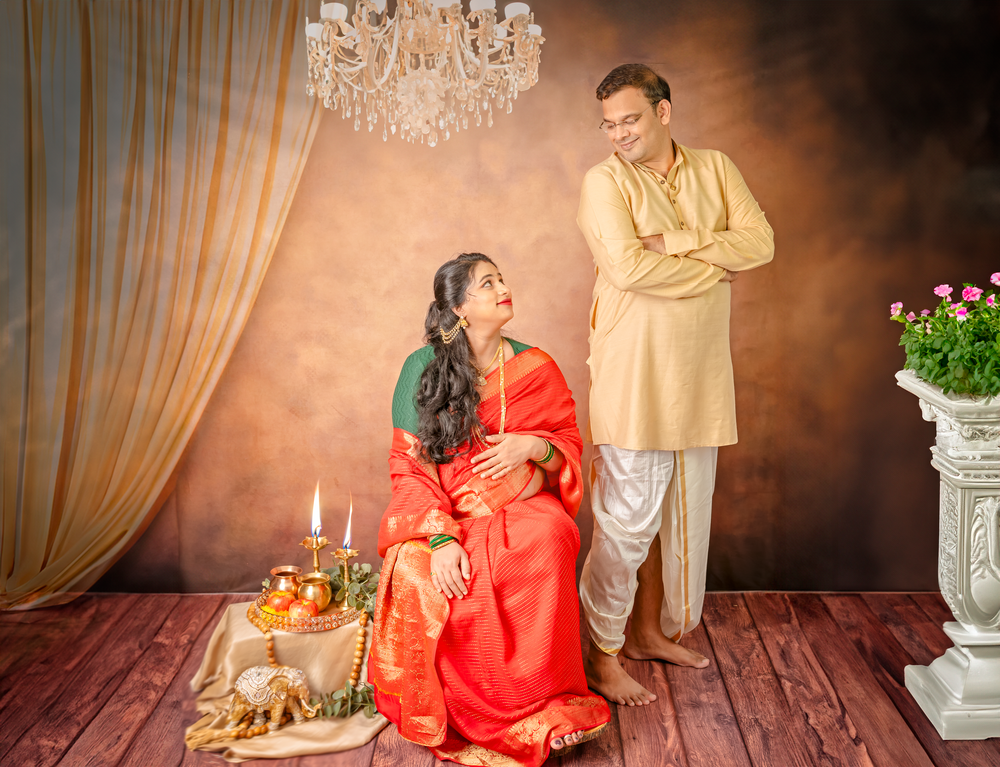 A couple in traditional Indian attire poses in a studio setting with elegant decor and lighting.