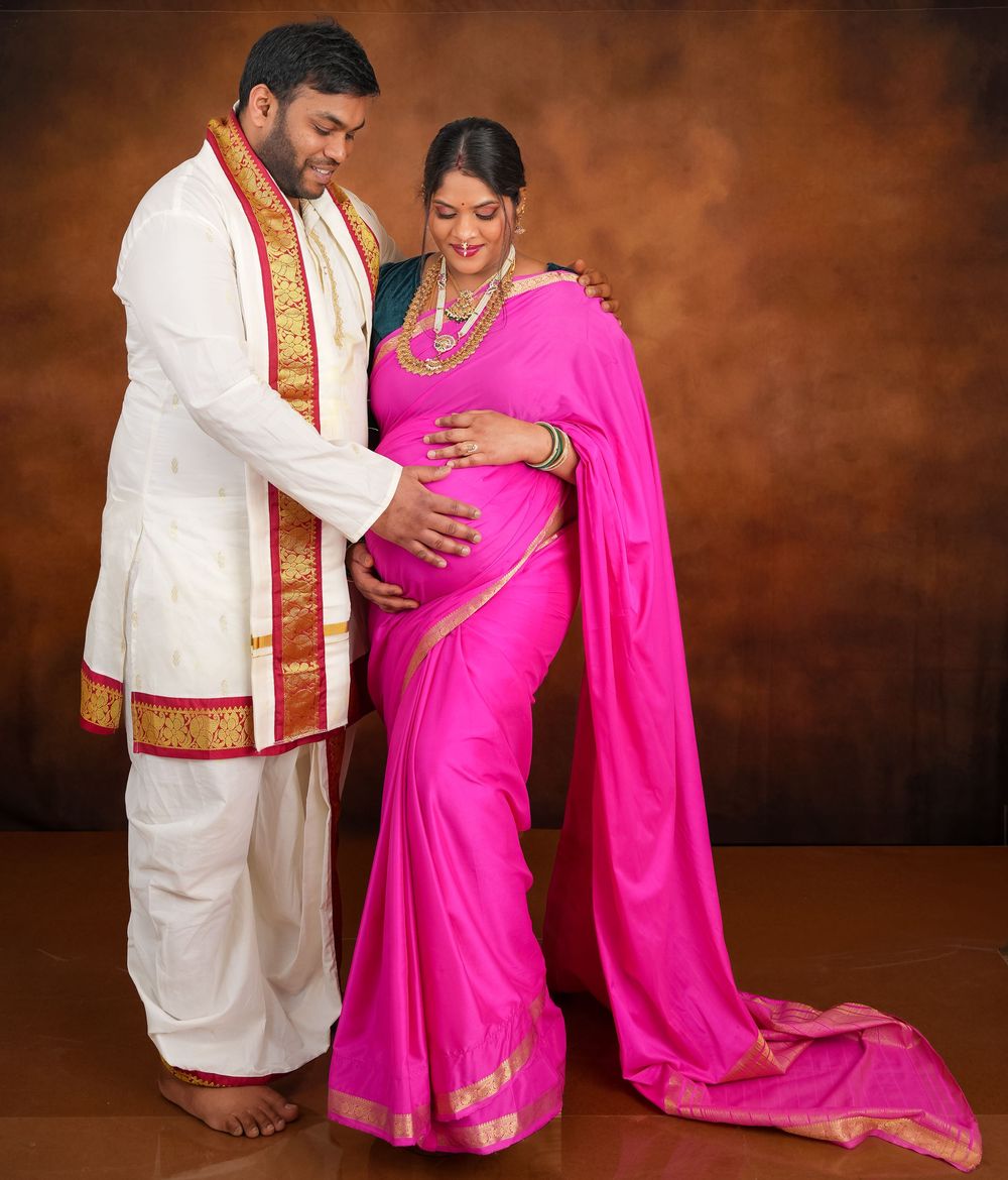 Elegant maternity portrait featuring bright pink saree and white traditional menswear.