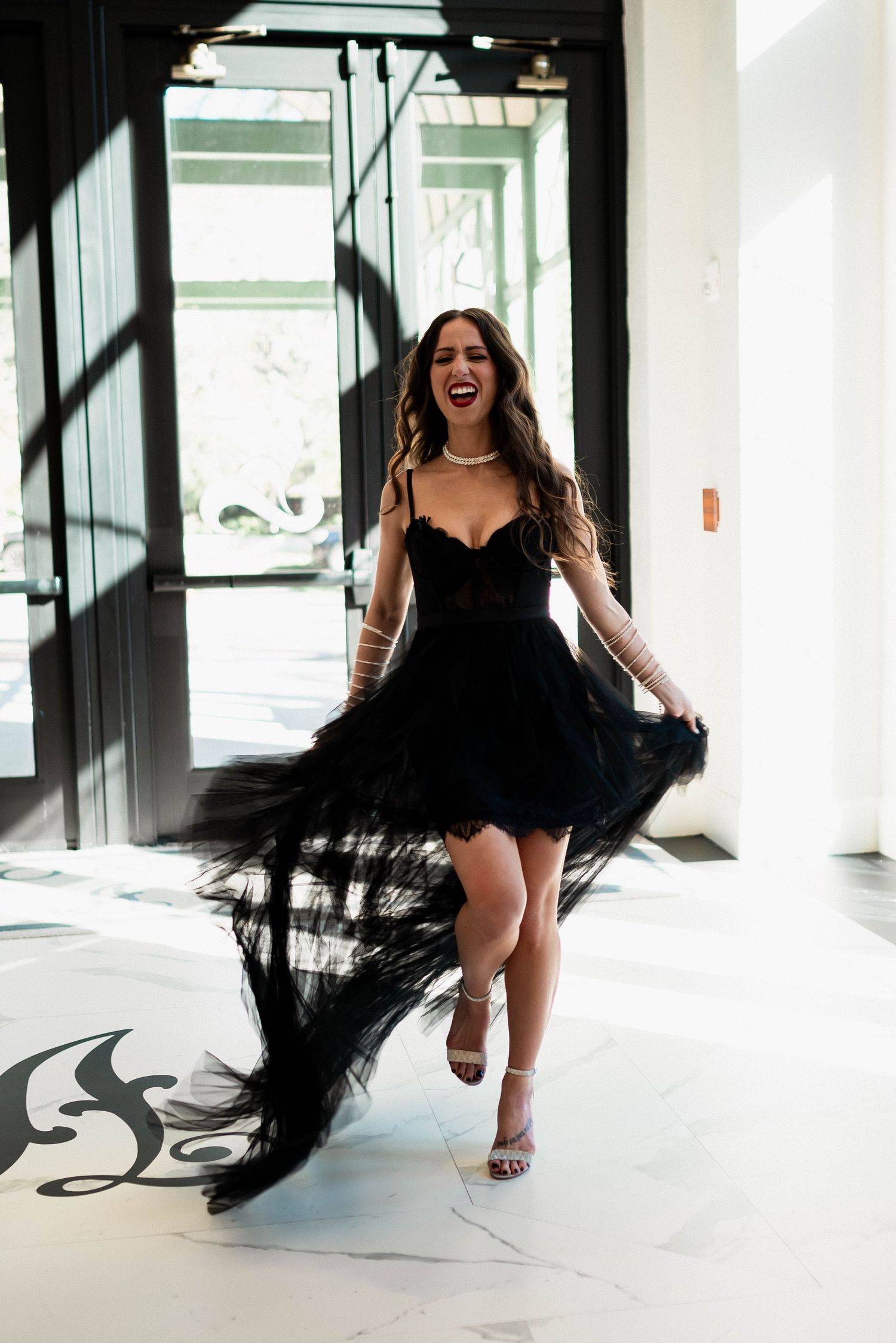 A twirling figure in an elegant black flowy dress dances in a bright interior space with dramatic shadows.