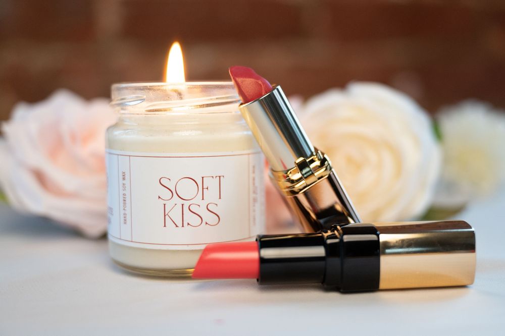 Glowing white candles and cosmetic products arranged with soft pink tones in a luxurious beauty flatlay setting.