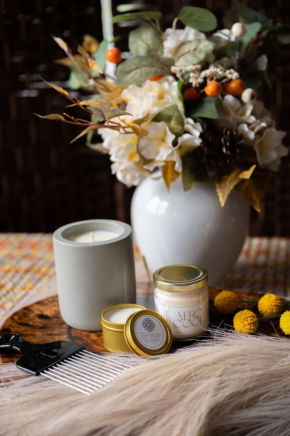 White ceramic vases with dried floral arrangements and gold accented candle jars on textured surface create a cozy home decor display.