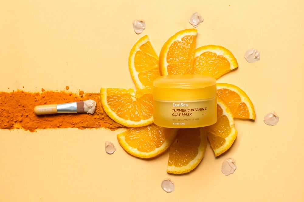 Orange skincare cream jar surrounded by fresh citrus slices and vitamin powder on yellow background.