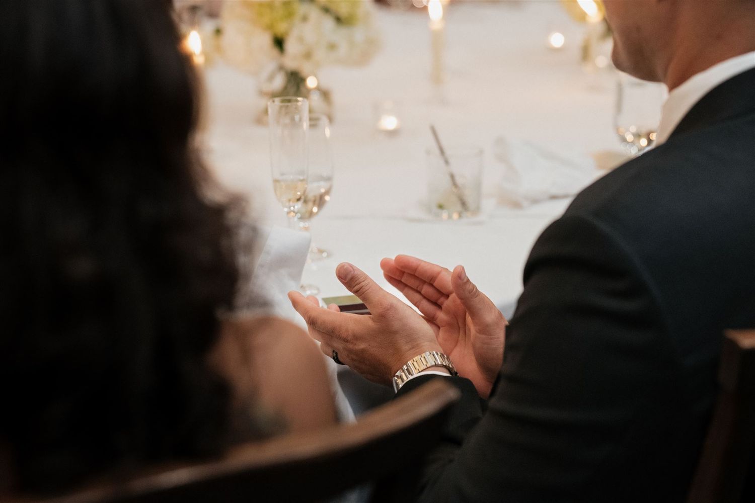 Two people in formal wedding attire hold hands during an intimate candlelit celebration.