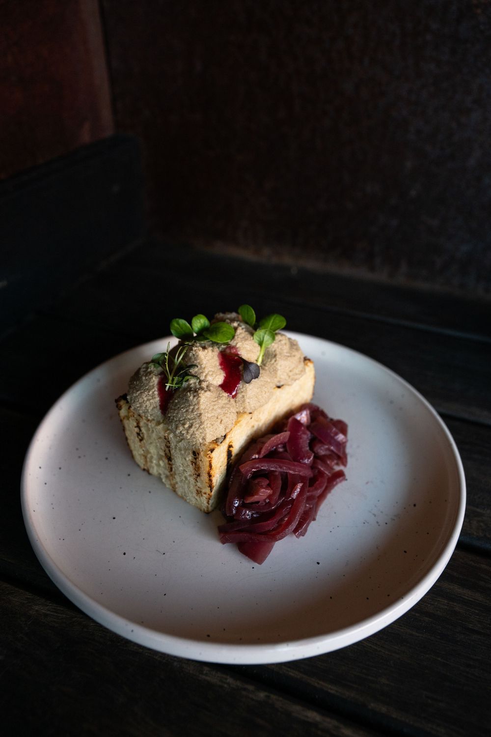 A slice of pate or terrine served with red cabbage garnish on a white plate in dramatic lighting.
