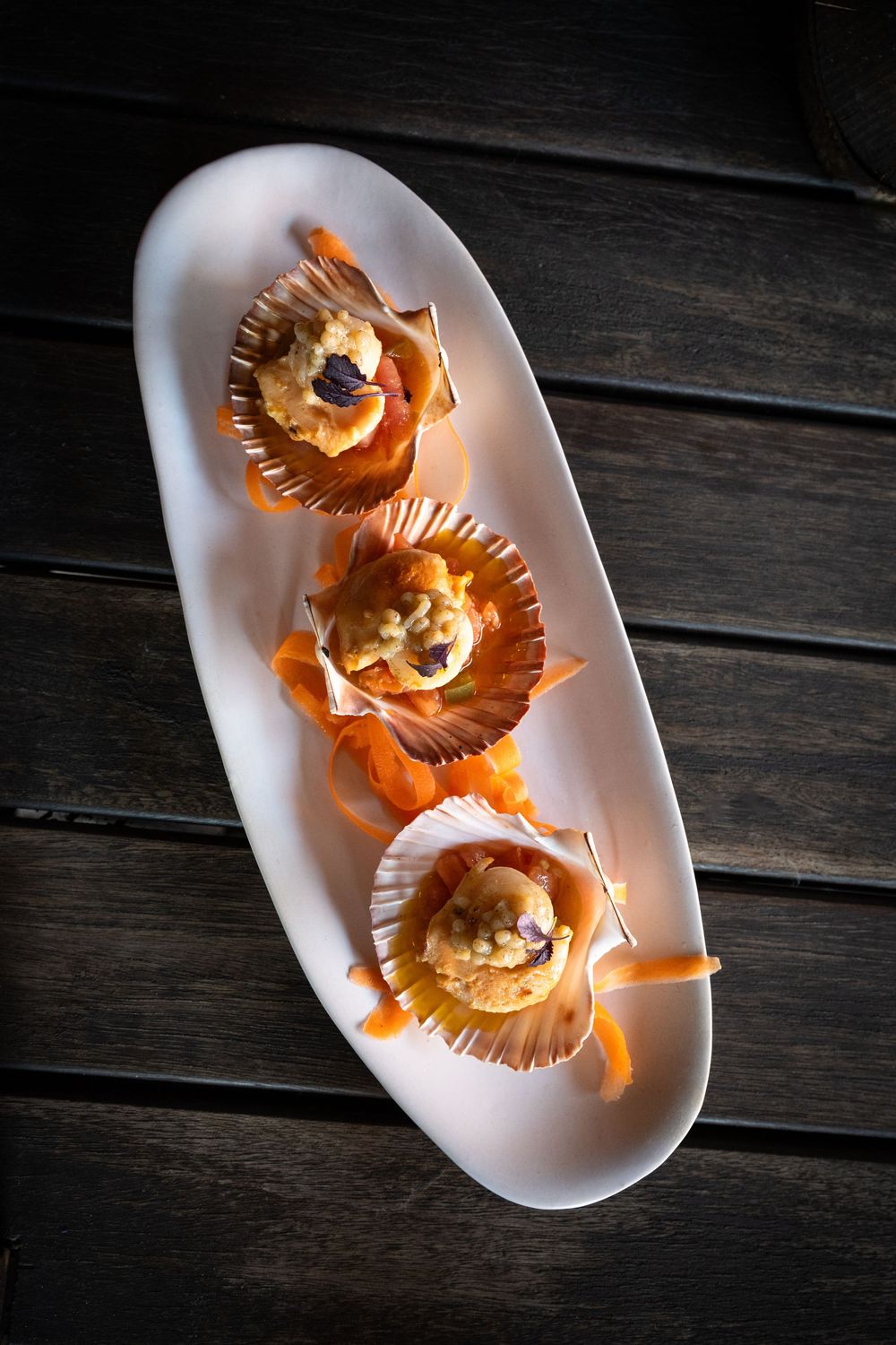 Three golden pastries arranged on white oval plate against dark wooden surface.