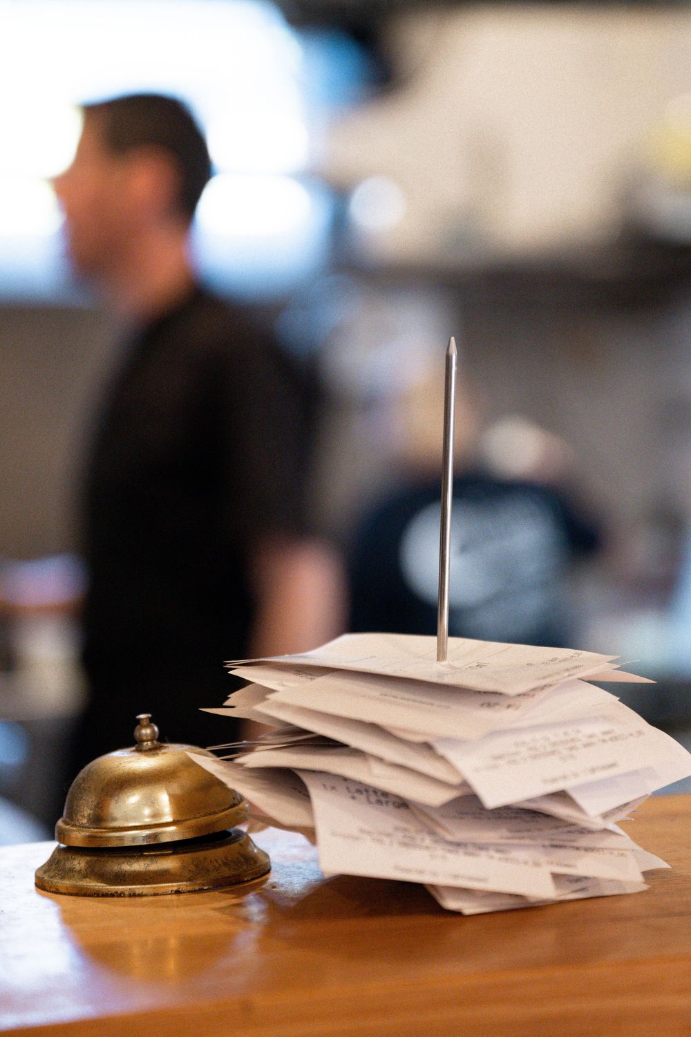 A brass service bell sits next to a stack of order tickets at a restaurant counter.