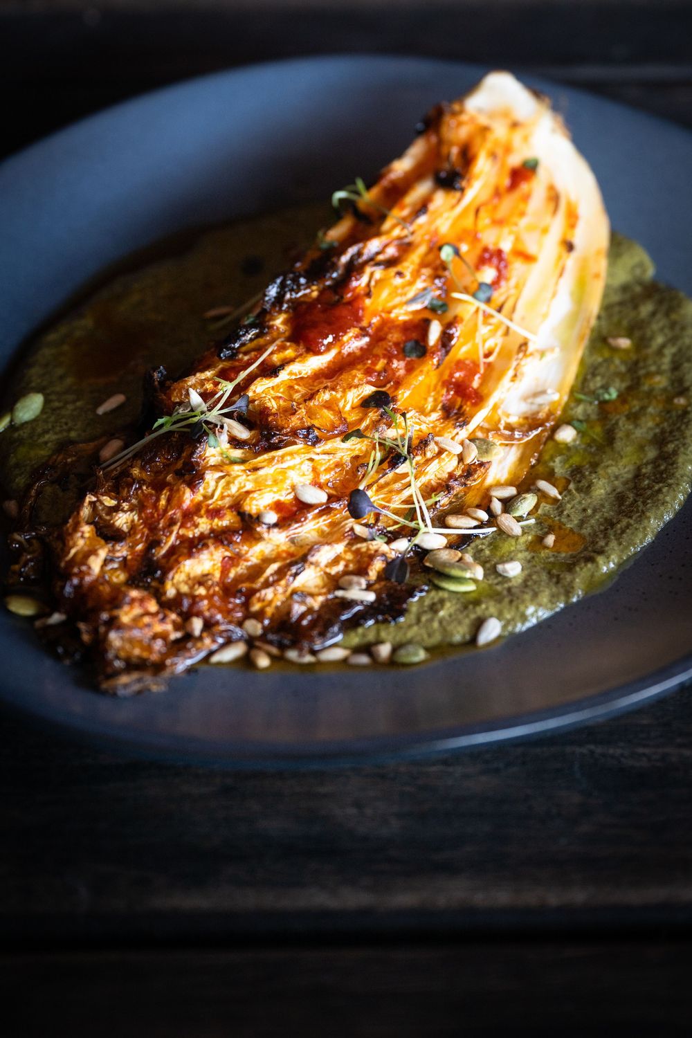 Four similar views of seared fish with pesto sauce plated on dark ceramic dishes with dramatic side lighting.