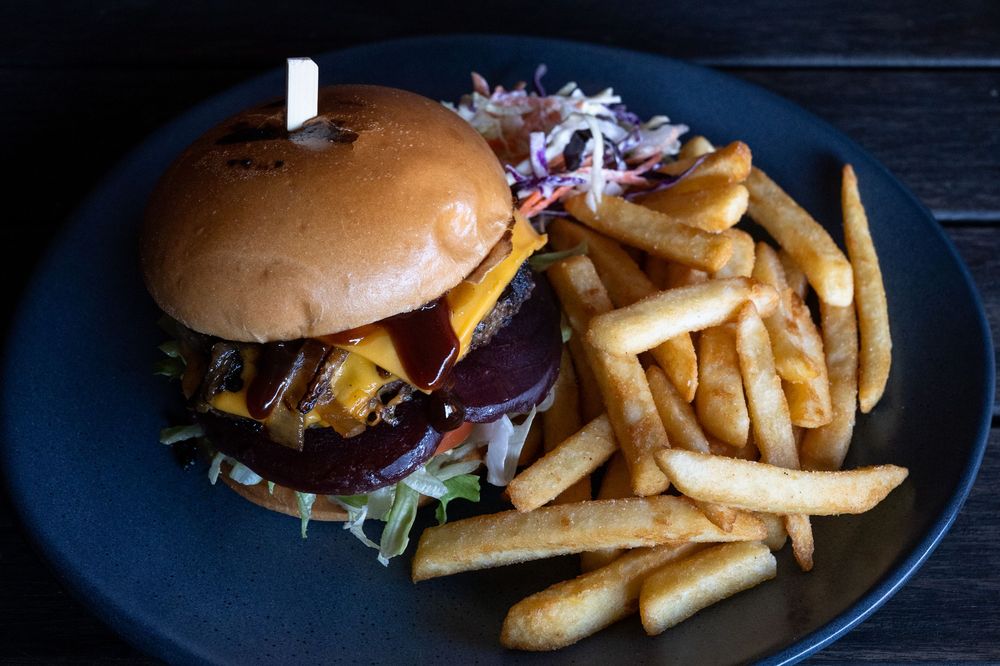 A cheeseburger with crispy french fries served on black plates against a dark background in sequence.