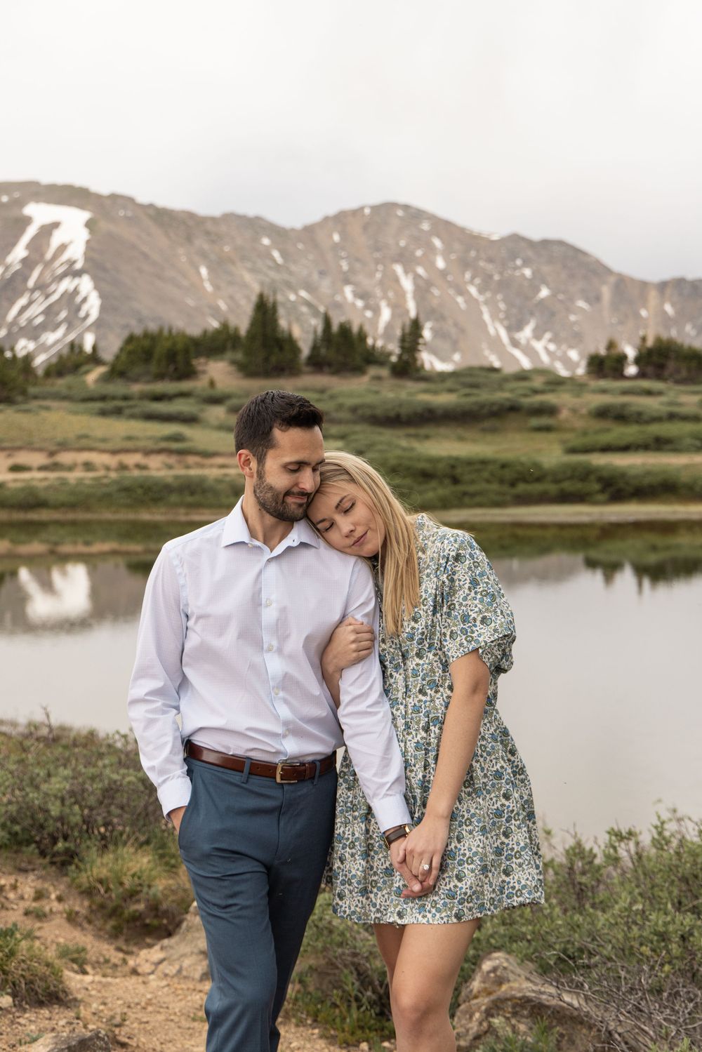 Moment between a couple by a serene mountain lake with rugged peaks in the background at Loveland Pass, Colorado..