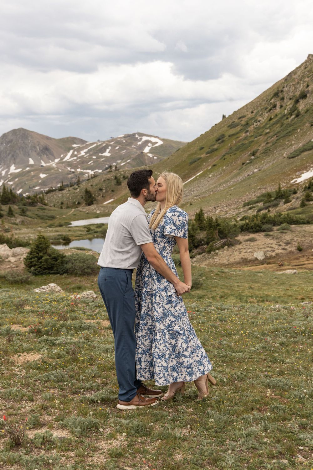 A romantic embrace in the Rocky Mountains with sweeping mountain vistas, wildflowers and alpine meadows in the background.