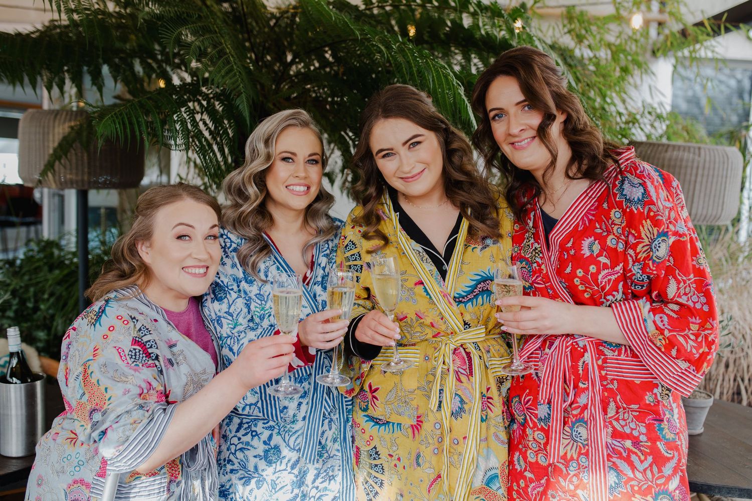 Four women in colorful floral robes smile and celebrate together at an indoor venue.