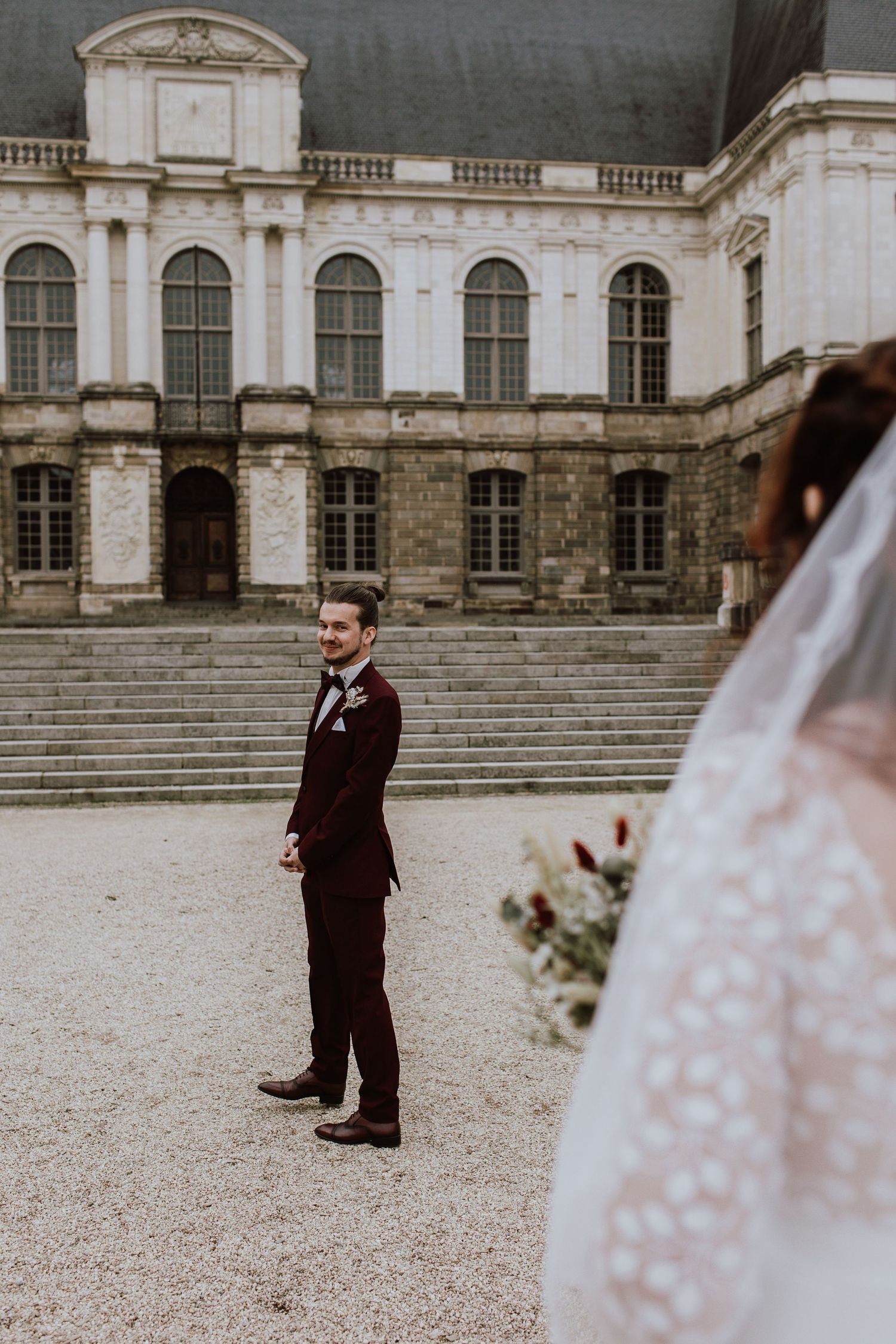 A wedding moment captured at a grand historic building with stone steps and arched windows on overcast day.