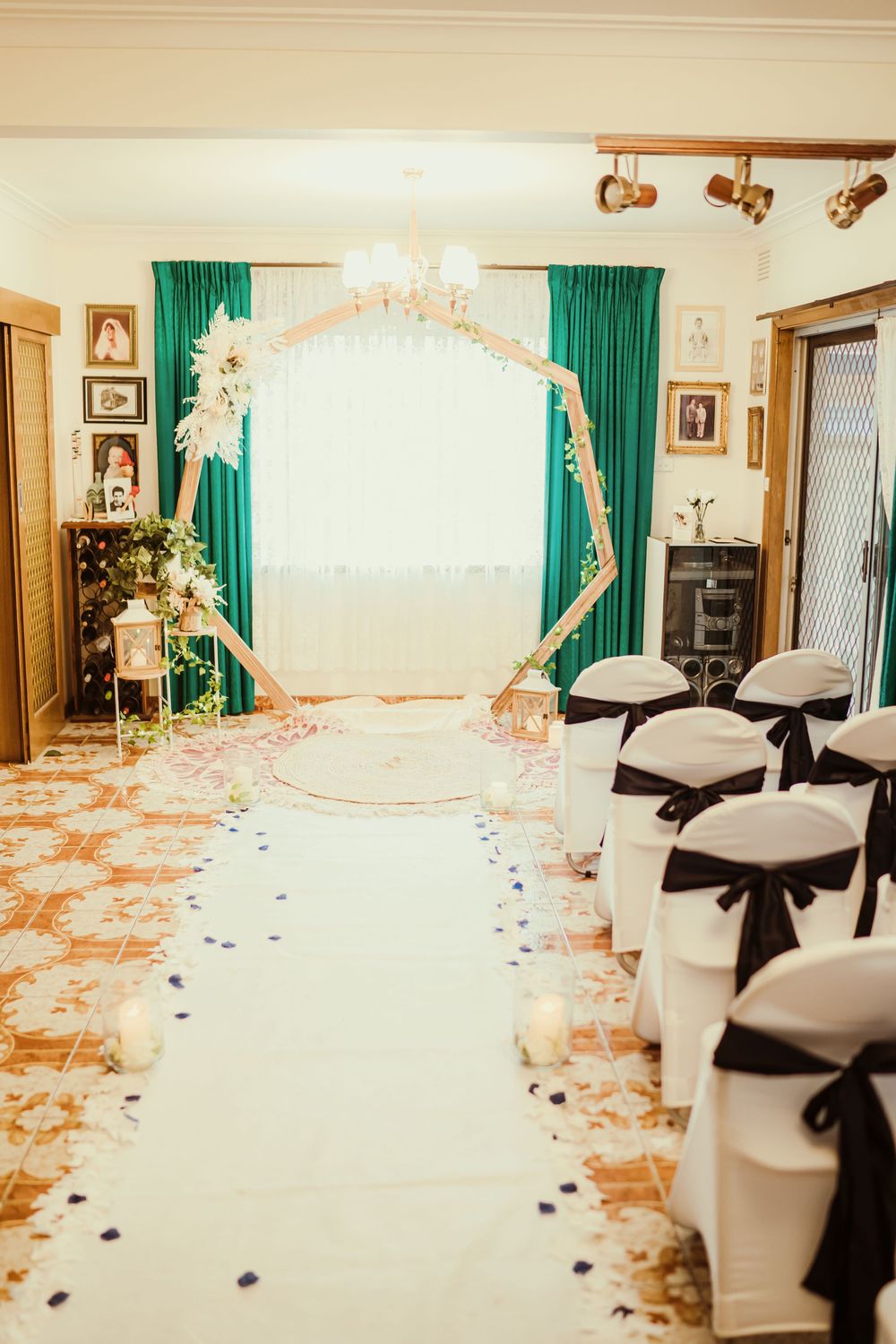 Wedding reception venue decorated with elegant white chair covers, green curtains, and romantic floral arrangements.