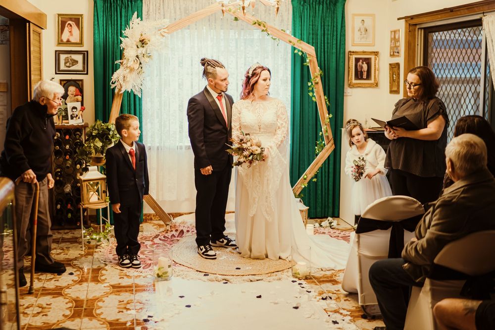 A wedding ceremony panorama showing guests gathered in a vintage room with emerald green curtains and wood paneling.