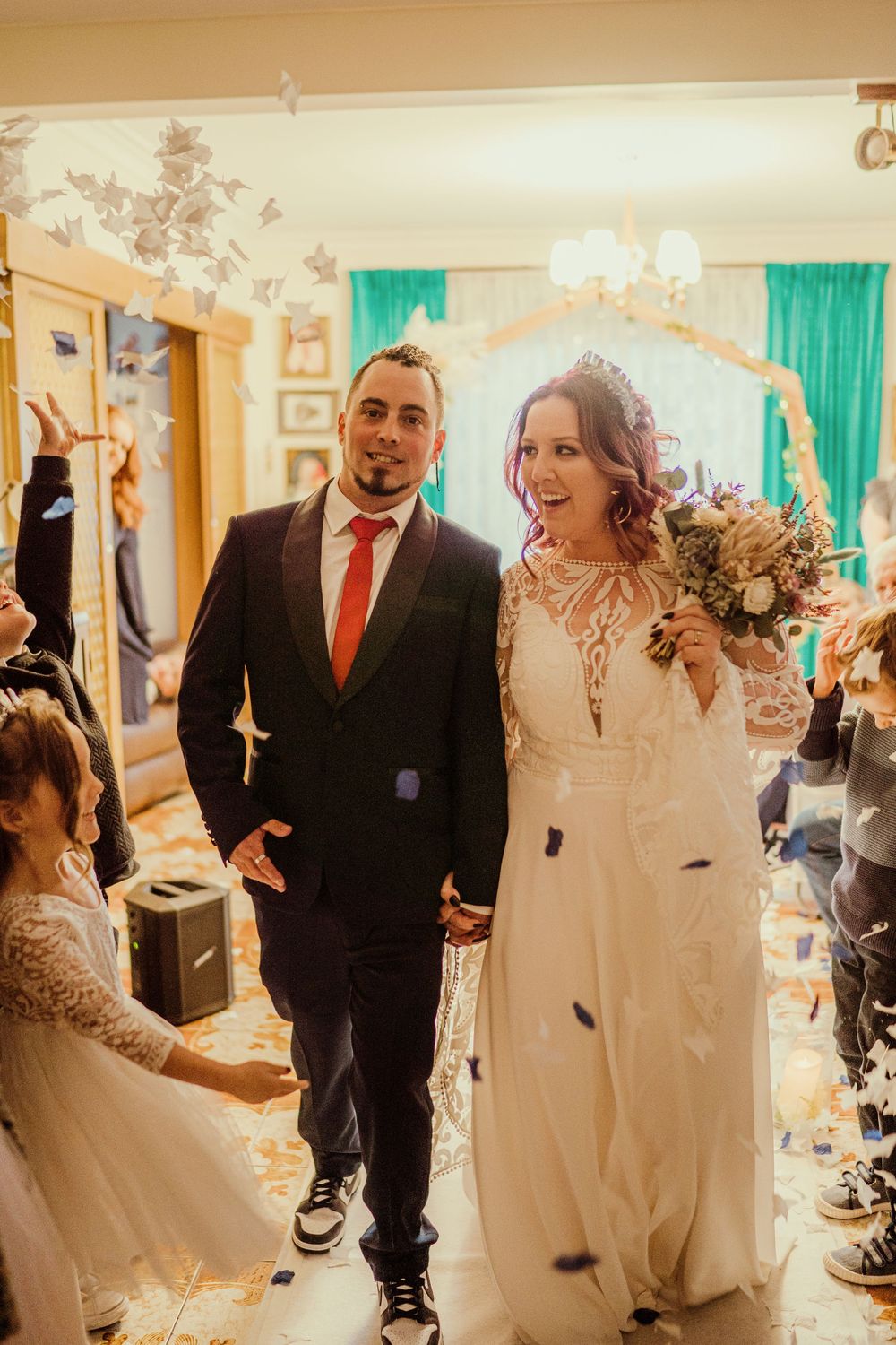 A joyful couple walks down the aisle at their wedding ceremony while confetti falls around them in a decorated indoor venue.