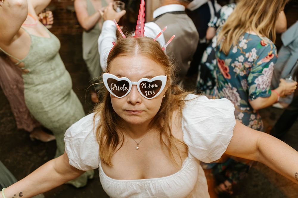 A group of people dancing at a lively wedding reception celebration with dresses and masks.