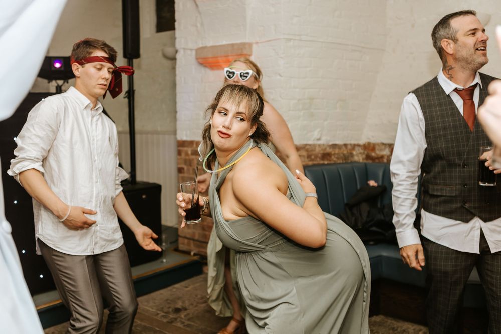 Wedding party guests dancing and enjoying themselves at a reception in a rustic indoor venue.