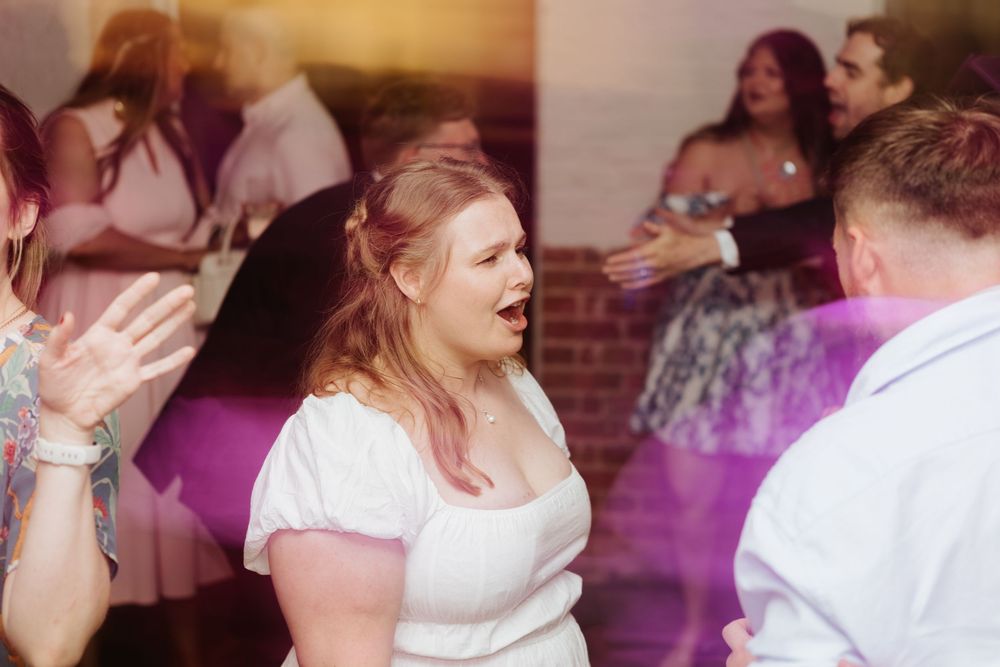People dancing and laughing at a wedding reception with purple lighting effects in the background.