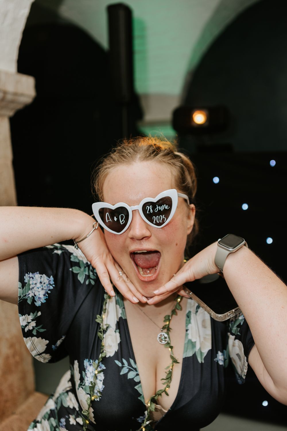 Sequence of fun photo booth shots showing someone in a floral dress wearing heart-shaped sunglasses making silly faces.