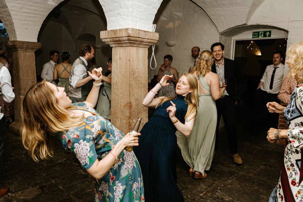 Wedding guests dance together in a historic stone venue during an evening reception celebration.