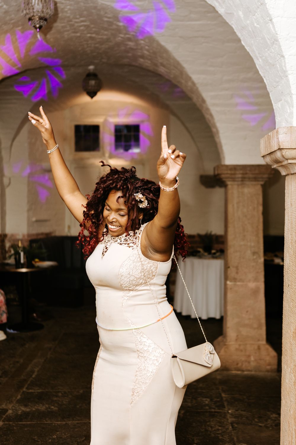 Series of joyful dance poses in a brick vaulted room with purple lighting by someone wearing an elegant white dress.