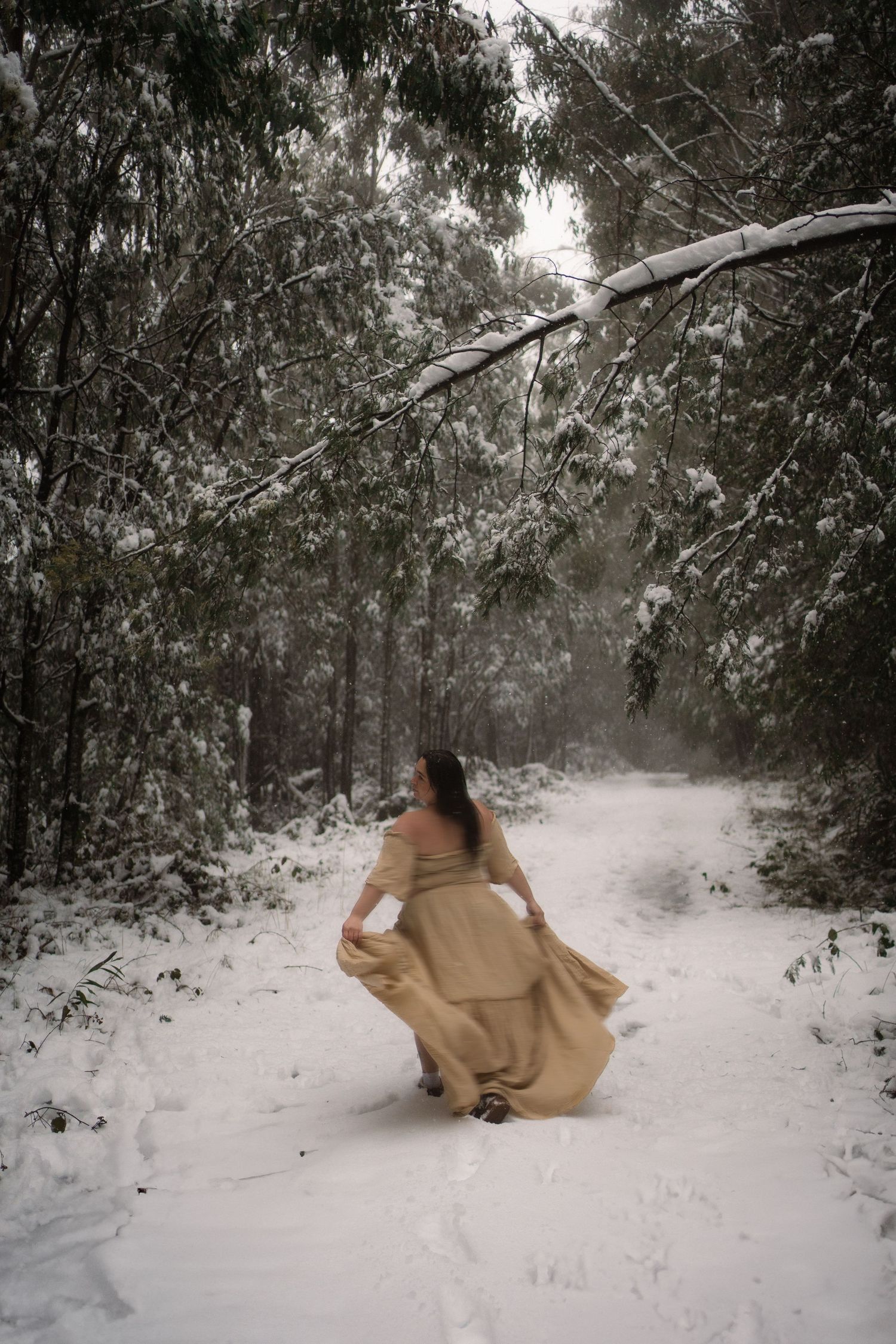 A figure in a flowing dress moves through a snowy forest path surrounded by winter trees and mist in Marysvlle, Victoria