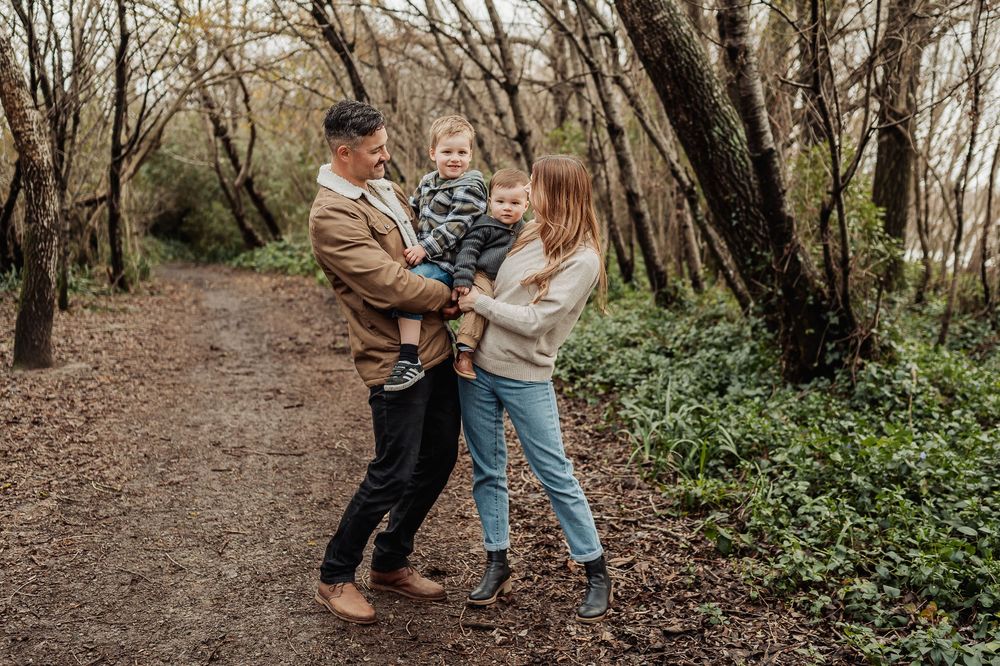 A family shares a joyful moment together while walking on a wooded trail surrounded by bare trees.