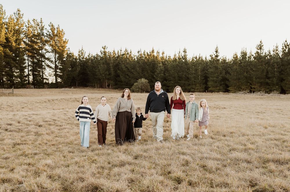 Family members walk together in a golden field during sunset as they pose for creative outdoor portraits.