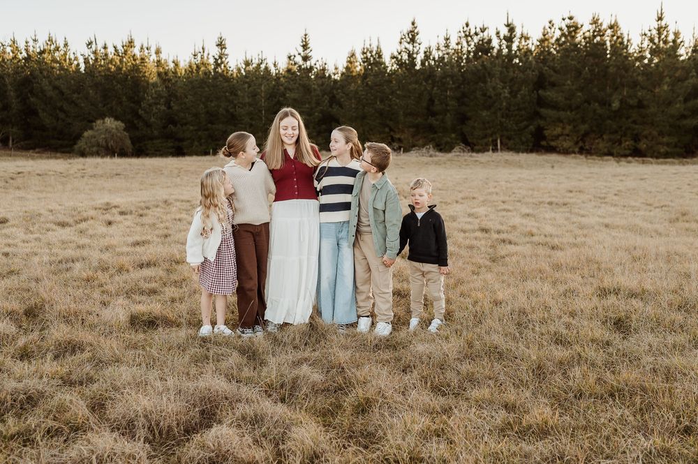 A group stands together in a golden grassy field at sunset with pine trees in the background.