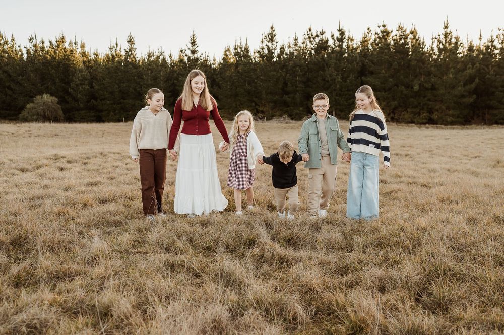 A group stands together in a rustic field at sunset wearing coordinated winter outfits in earth tones and stripes.