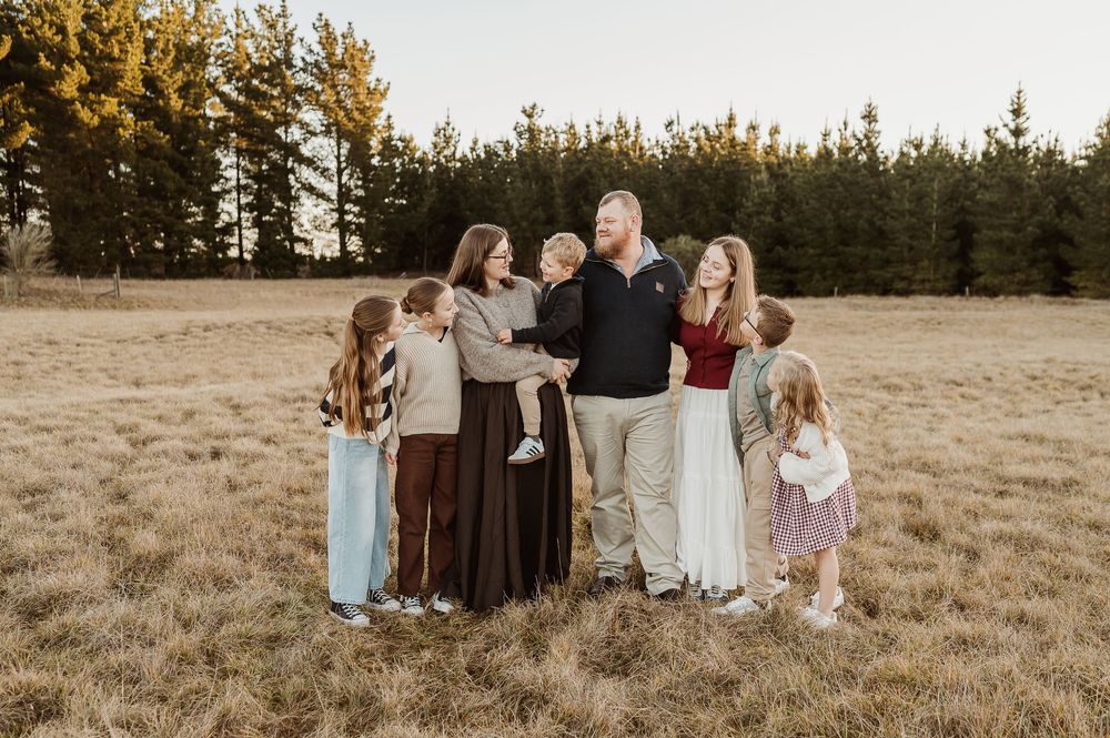A group stands together in a golden field at sunset with evergreen trees in the background.