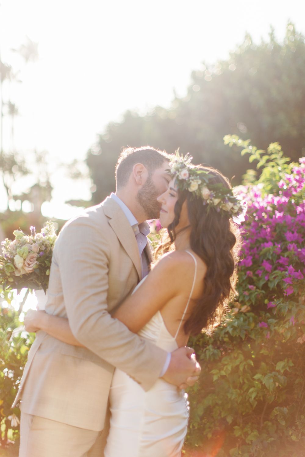 Romantic couple shares a loving kiss at sunset in a garden with blooming pink flowers and golden sunlight.