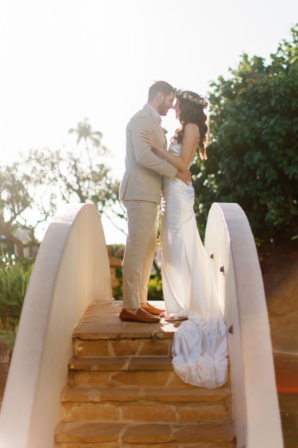 A couple shares a romantic moment at sunset on stone steps with white railings at a tropical resort location.