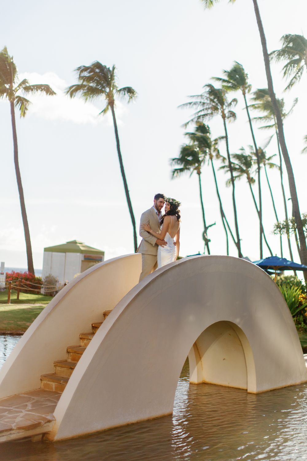 White arched bridges over calm water with palm trees swaying in the wind at a tropical resort.