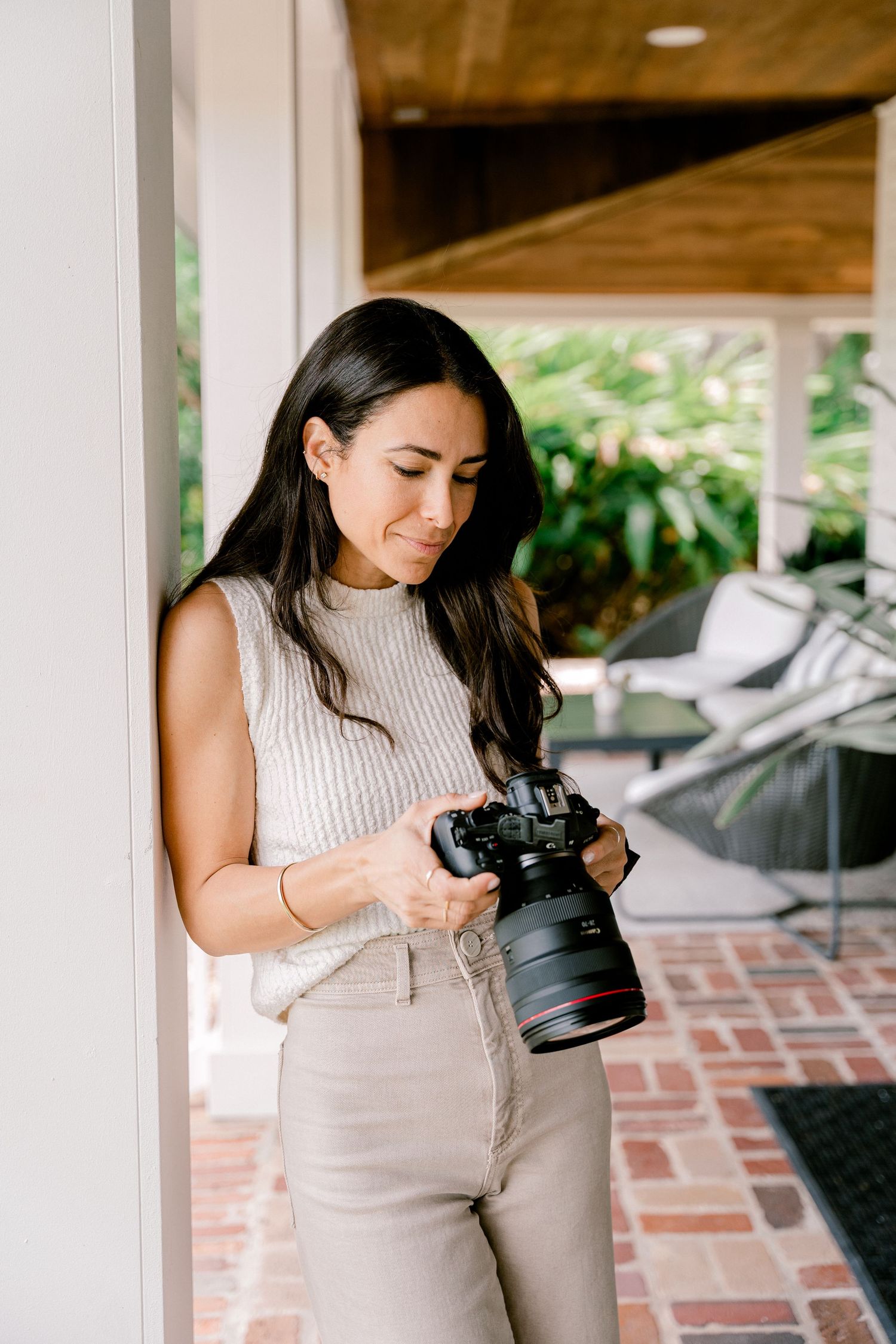 Photographer wearing cream sweater checking camera settings in outdoor setting.