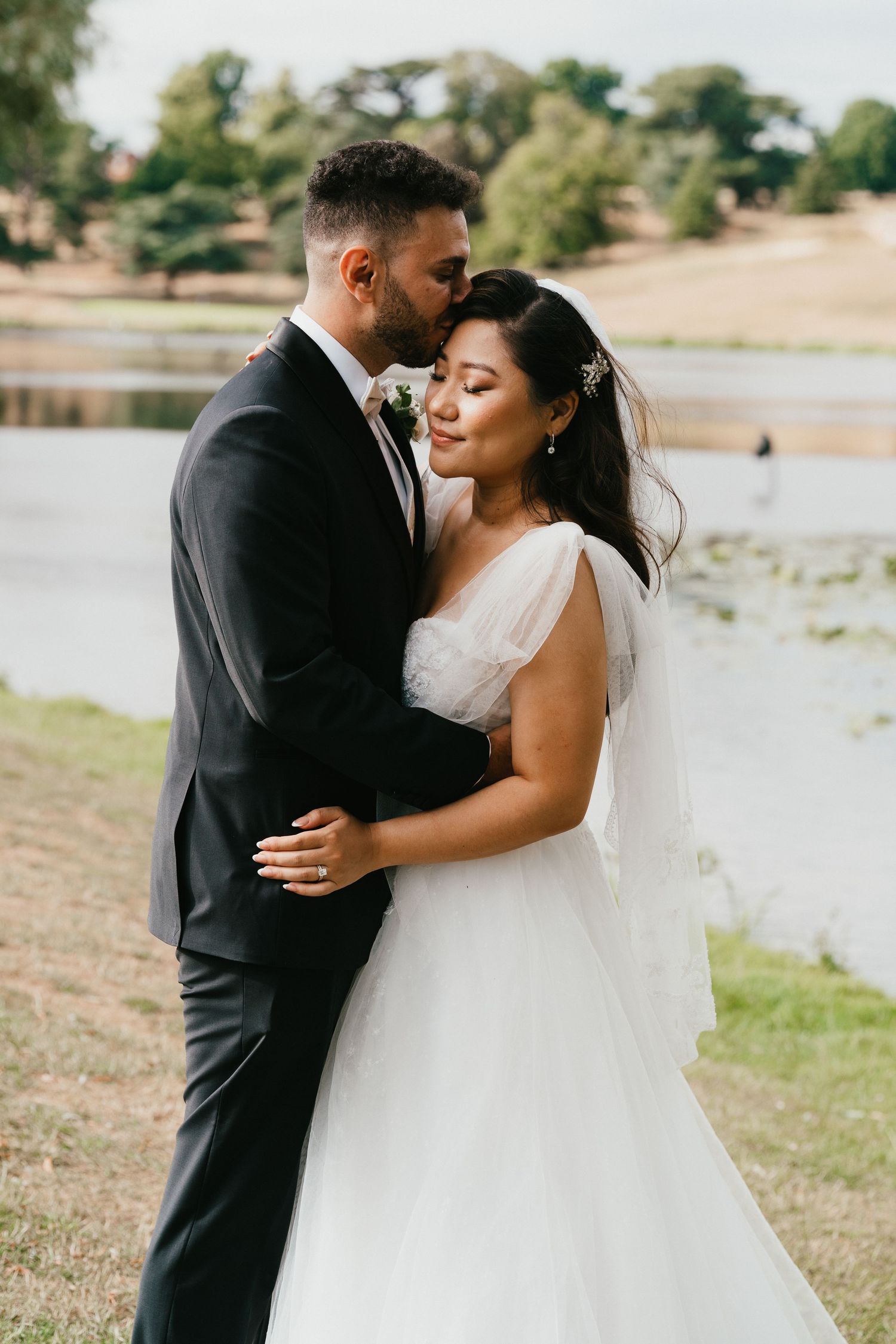 A romantic wedding portrait of a couple embracing by a lakeside on their special day.