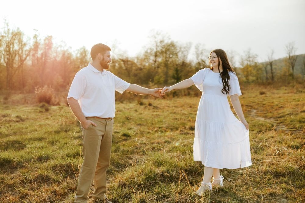 A couple stands in a sunlit golden field during sunset creating a romantic silhouette against the warm sky.