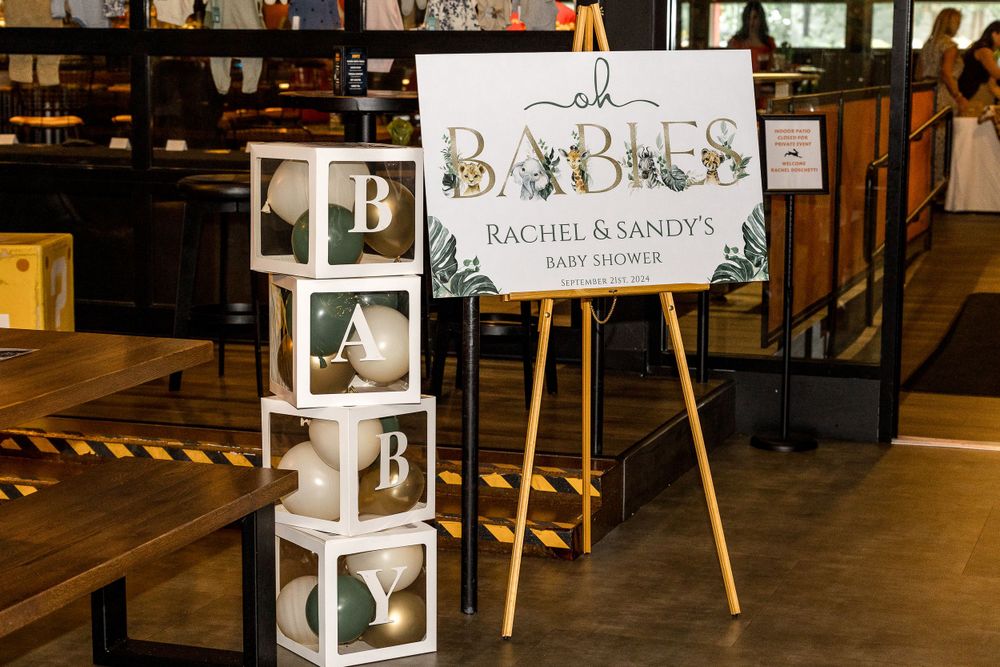 Baby shower welcome sign and photo display cubes arranged on wooden table.