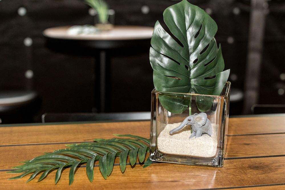 A tropical monstera leaf in a glass vase on wooden table.