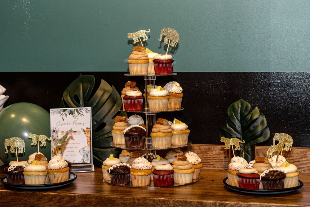 Cupcake display featuring decorative safari animal toppers on tiered stands with monstera leaves and party decor.