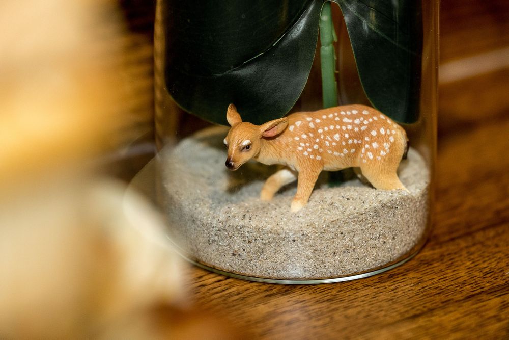 Small decorative deer figurine displayed in a glass jar filled with sand.