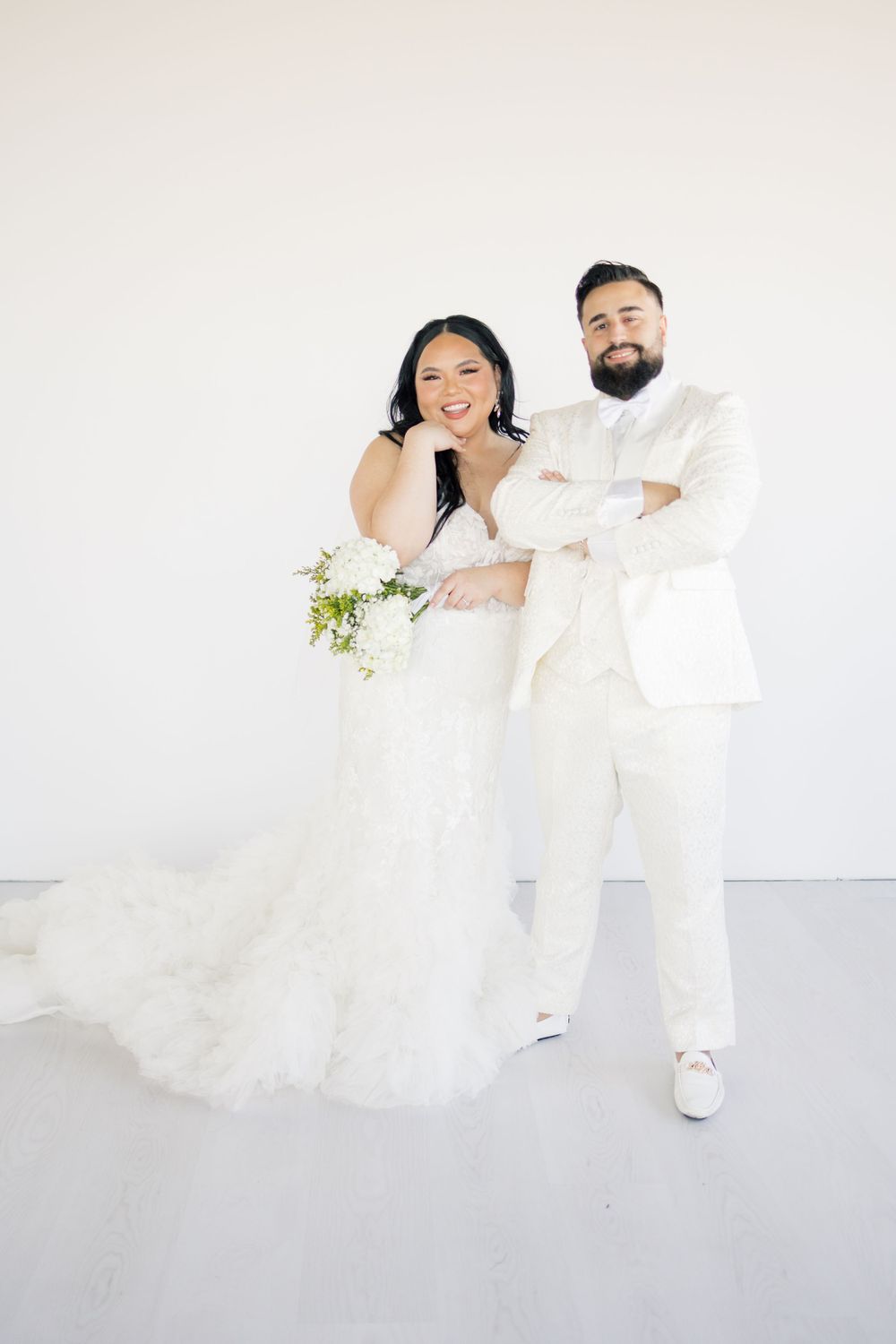 Wedding portrait of couple in all-white attire against minimal white background.