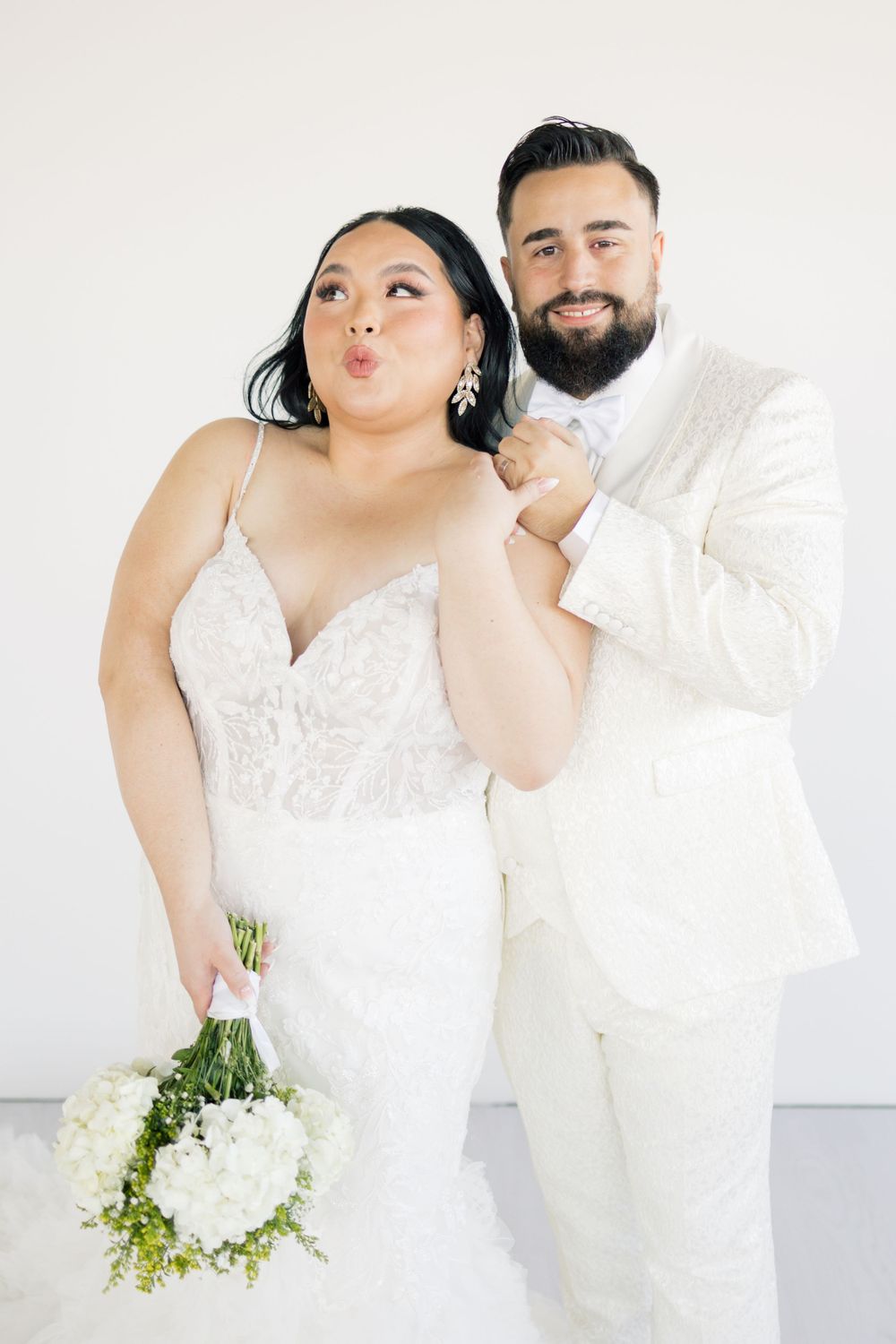 Playful wedding portrait of couple in white outfits making fun expressions.