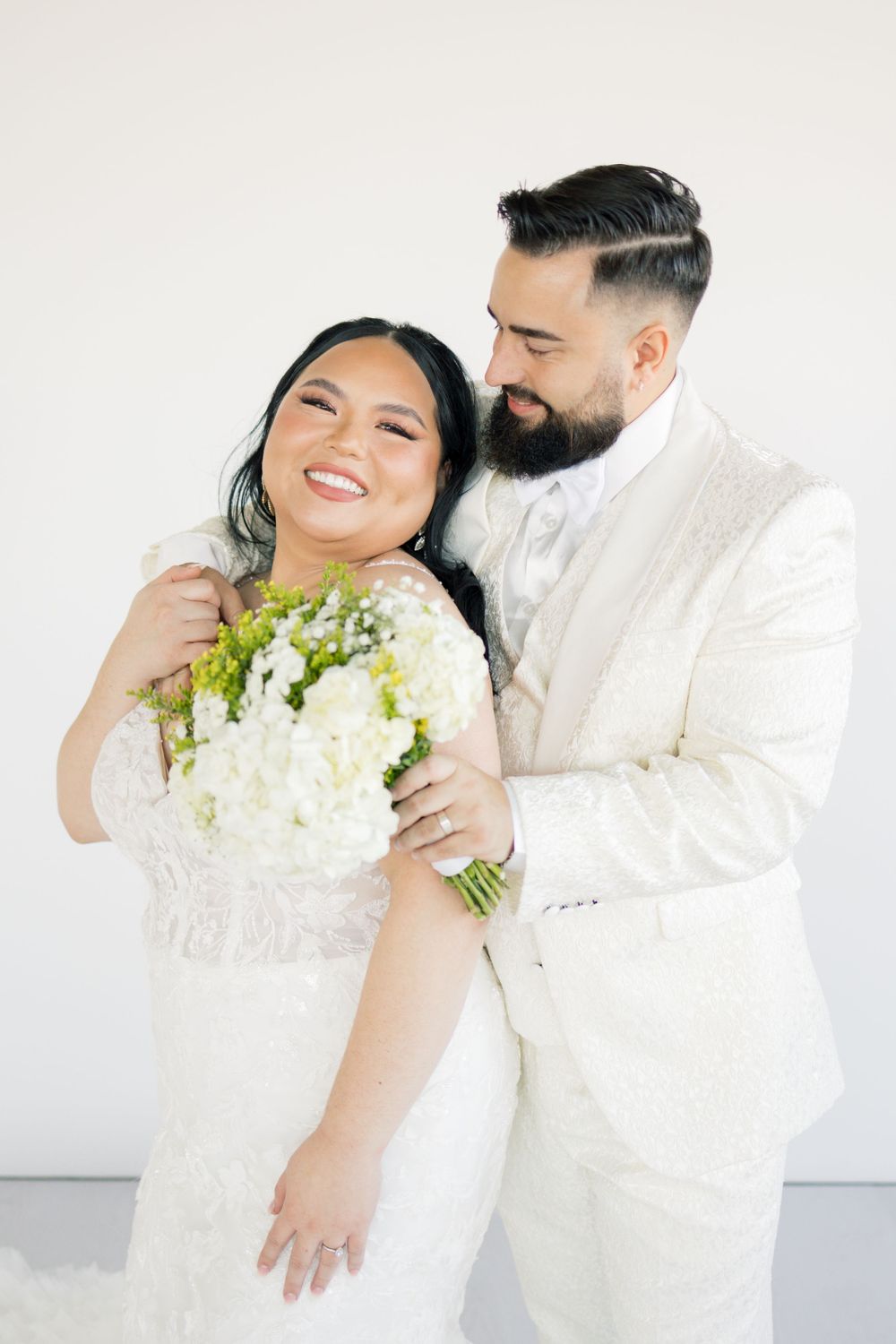 Joyful wedding couple sharing a candid moment with white floral bouquet.