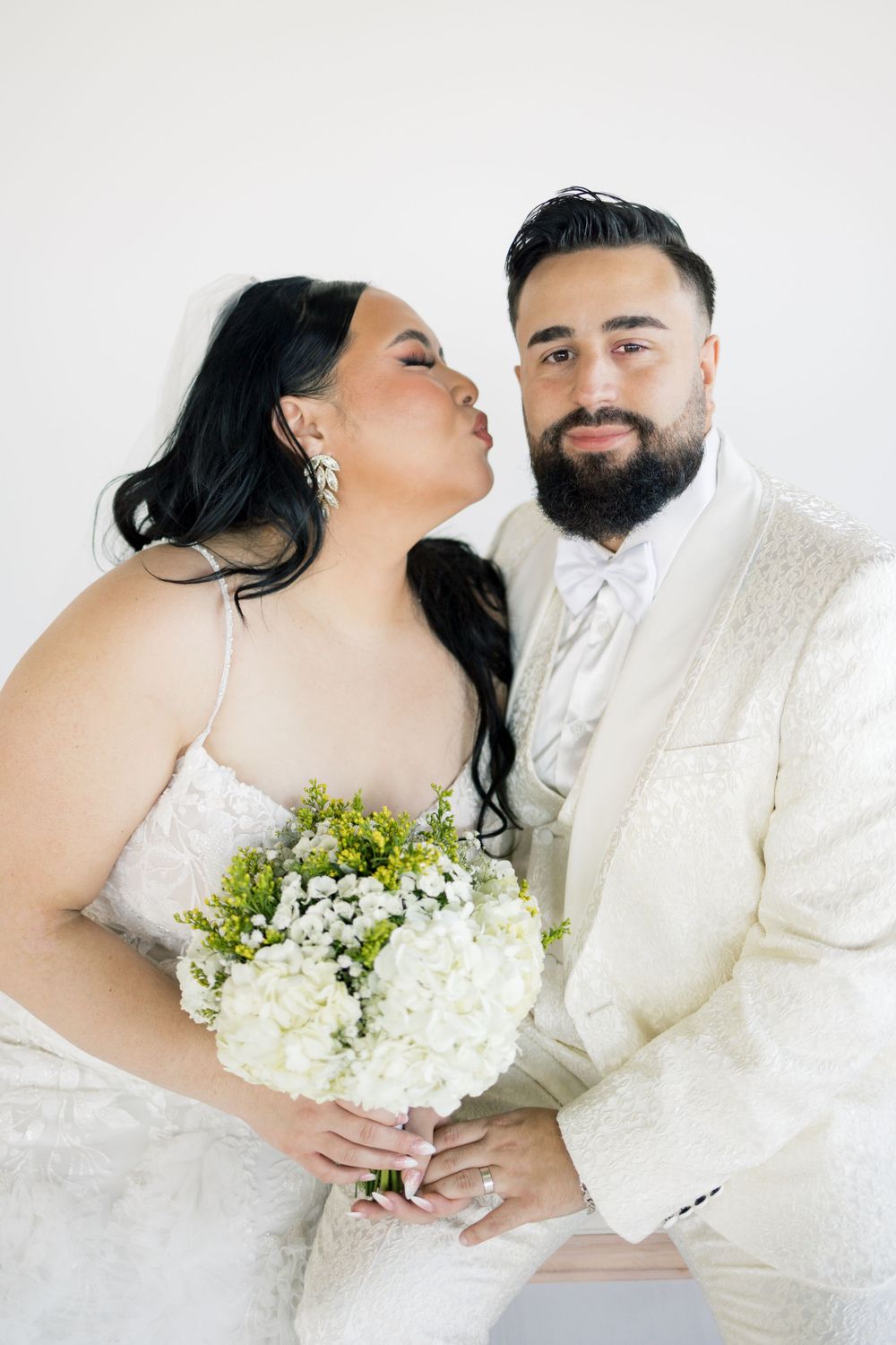 Intimate wedding portrait of couple in white with bride holding hydrangea bouquet.