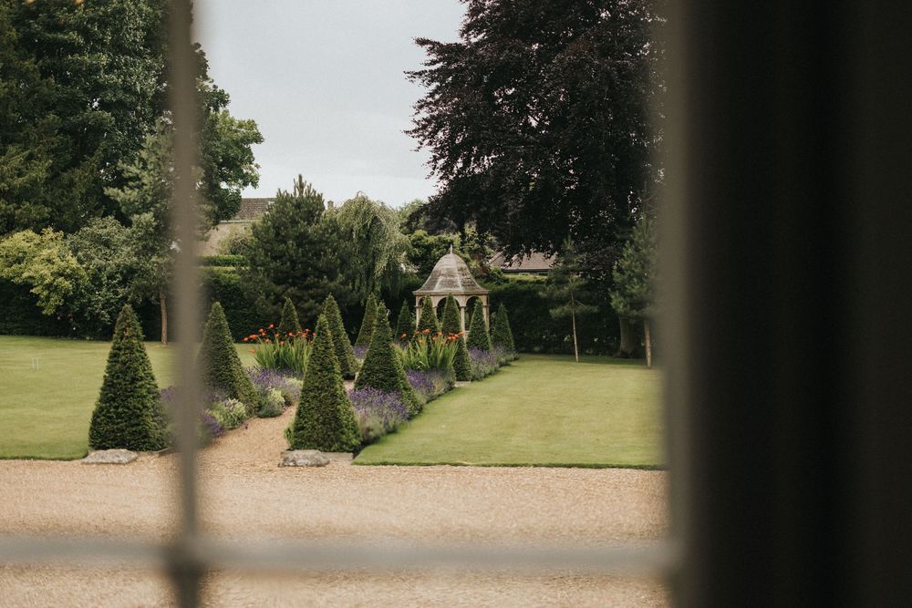A tree-lined garden path leads to a classical English country estate with manicured hedges at Washingborough Hall.