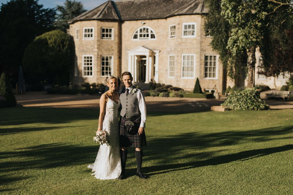 Couple strolling on a sunlit mansion lawn surrounded by elegant architecture at Washingborough Hall - taken by Grimsby photographer.