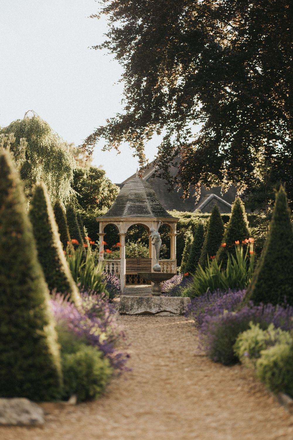 A wooden gazebo stands at the end of a garden path lined with purple lavender and evergreen topiaries at Washingborough Hall.