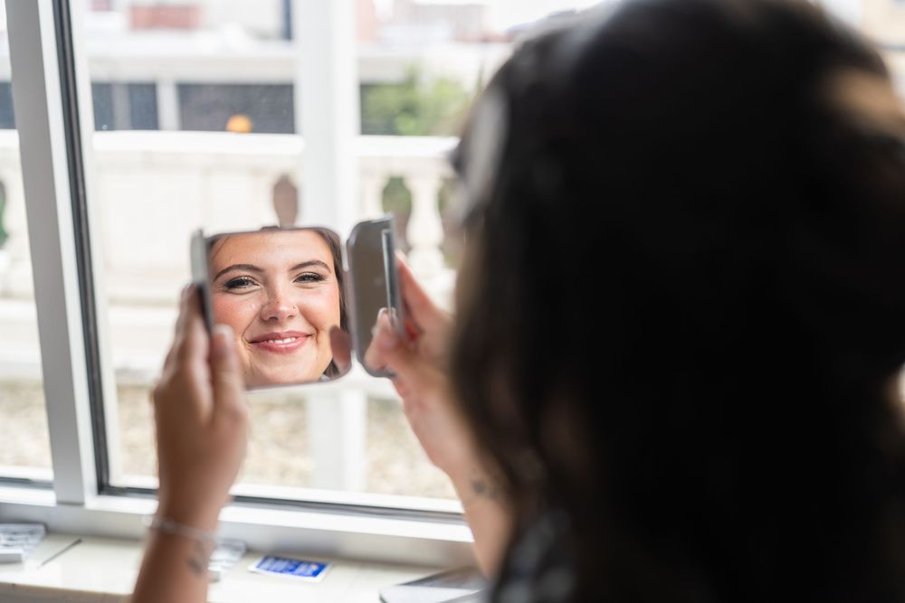 Someone admires their reflection while holding up a small mirror near a bright window.