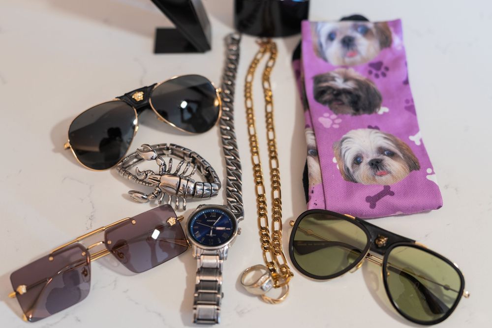 A collection of stylish sunglasses, chains, and accessories laid out on a light surface with a pink patterned cloth.